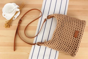 Detail of woven mesh bag with brown leather strap on light wood background