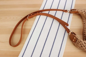 Detail of brown PU leather shoulder strap and golden metal buckle on woven bag