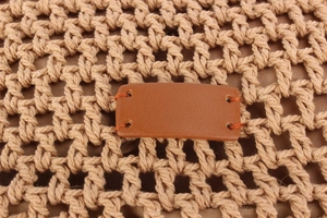 Macro detail of the woven fiber mesh and brown leather tag on a stylish casual handbag