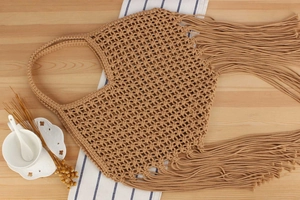 Close-up of khaki mesh woven bag with fringe detail on a natural wood background