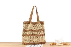 Macro detail of large straw tote bag with brown leather straps and striped woven texture