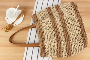 Close-up of beige and brown striped woven tote bag with crochet texture on wood surface