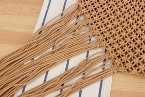 Close-up of khaki mesh woven bag with long tassels on a light wooden background