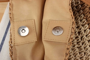 Detail of hand-woven straw bag featuring a silver magnetic snap button and fabric lining