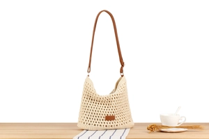 Detail of cream woven shoulder bag with brown leather strap on a rustic wooden table