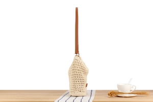Detail of beige crochet shoulder bag with brown leather strap in a minimalist setting