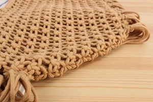 Detail shot of hand-woven hollow mesh structure and natural tassel fringe on this handbag