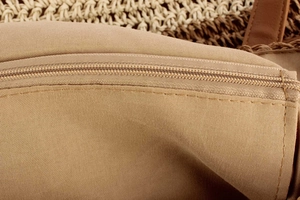 Detailed close-up of khaki fabric lining and smooth zipper closure on woven shoulder bag