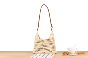 Detail of off-white hollow woven bag with brown leather strap on a wooden table