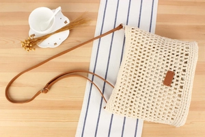 Detail view of beige crochet woven tote with brown leather strap and decorative leather patch