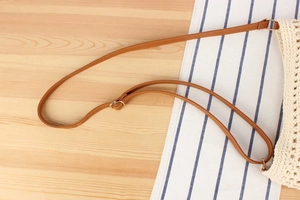 Close-up of a woven bag showing a brown leather strap and golden metal buckle details