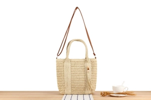 Detail of beige woven straw tote bag with dark brown straps and tassel charm on a table