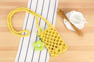 Detail of yellow woven cotton rope phone bag with green flower charm and crossbody strap