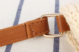 Close-up of brown leather strap and gold metal ring on woven off-white shoulder bag