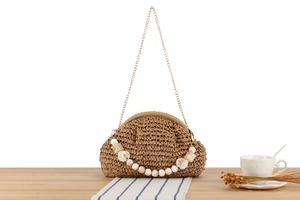 Detail of khaki woven crossbody bag with resin beads and gold chain on wooden table