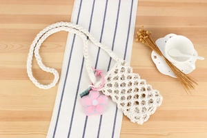 Close-up of beige woven cotton phone bag with pink flower charm on wooden surface