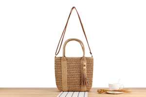 Detail of woven straw tote bag with brown leather handles and decorative tassel ornament