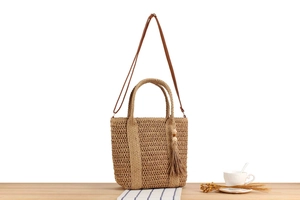 Detail of woven straw handbag with wooden bead tassel and brown shoulder strap