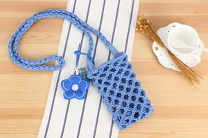 Detailed grid weave of blue woven cotton phone bag with floral charm on table