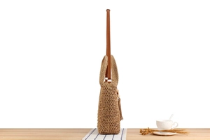 Close-up of a woven straw handbag with brown leather straps and wooden bead tassel detail
