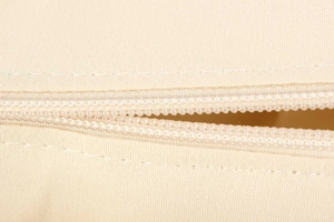 Close-up of a smooth nylon zipper and thick woven canvas texture on a beige handbag