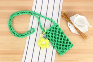 Green handmade woven cotton phone bag with yellow flower charm on wooden background