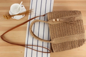 Top view of woven straw tote bag with tassels and leather strap on wooden table