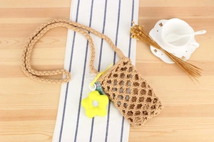 Detail of woven cotton cell phone bag with floral charm on a rustic background