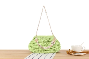 Dettaglio borsa intrecciata verde chiaro con perline di marmo e catena oro su legno
