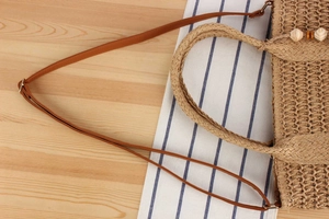 Detail of woven straw handbag with adjustable leather strap and decorative wooden beads