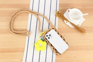 Detail of woven cotton phone bag featuring a yellow flower charm on a wooden desk