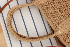 Detailed close-up of natural straw weave texture and sturdy handle on woven tote bag