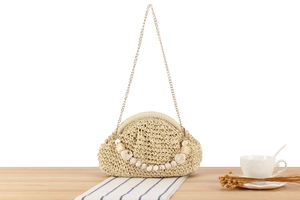 Detail of woven straw handbag with marble texture beads and metal chain on wooden desk
