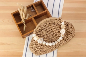 Detail of woven straw bag with marble acrylic beaded handle on a rustic wooden table