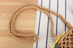 Detail of hand-woven cotton rope handle with floral tag and yellow hardware on bag