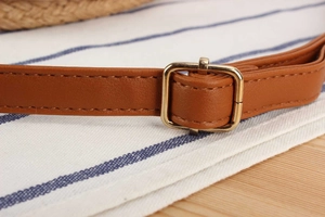 Detail of caramel leather strap with gold buckle and stitching on woven bag