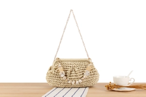 Dettaglio borsa intrecciata beige con perline effetto marmo e catena dorata su legno