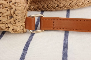Detail of brown leather strap and gold buckle on a natural woven straw tote bag