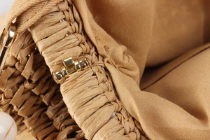 Detail of woven straw bag showing golden buckle, khaki fabric lining and zipper texture