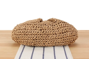 Close-up of beige woven clutch bag with natural texture on a wooden table setup