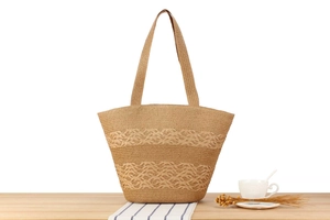 Detail of light brown woven straw tote bag with scalloped openwork patterns and long straps