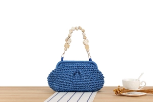 Detail of blue woven handbag with marble-textured beaded handle on a wooden table