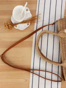 Flat lay of a woven straw handbag with leather strap on a rustic wood and striped background