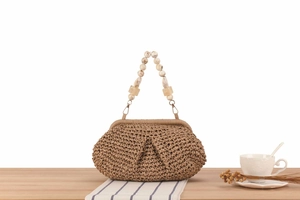 Detail of woven straw bag with marble-effect beaded handle on a wooden table