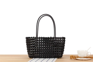 Detail of a black hollow woven basket bag featuring glossy texture on a wooden table