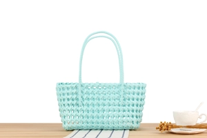 Detail of mint green woven basket bag with hollow pattern on a wooden table