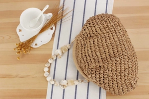 Detail of hand-woven straw handbag featuring marbled resin bead handles and gold clasp