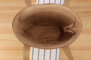 Detailed interior of woven straw tote bag showing brown lining and functional zipper pocket
