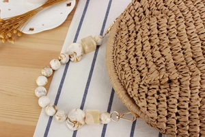 Detail of round straw bag featuring marble resin bead strap and golden metal hooks