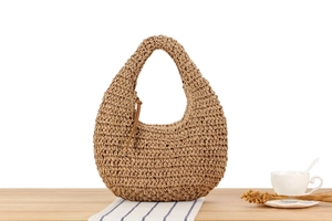 Detail of hand-woven straw tote with leather tie charm on a rustic wooden table
